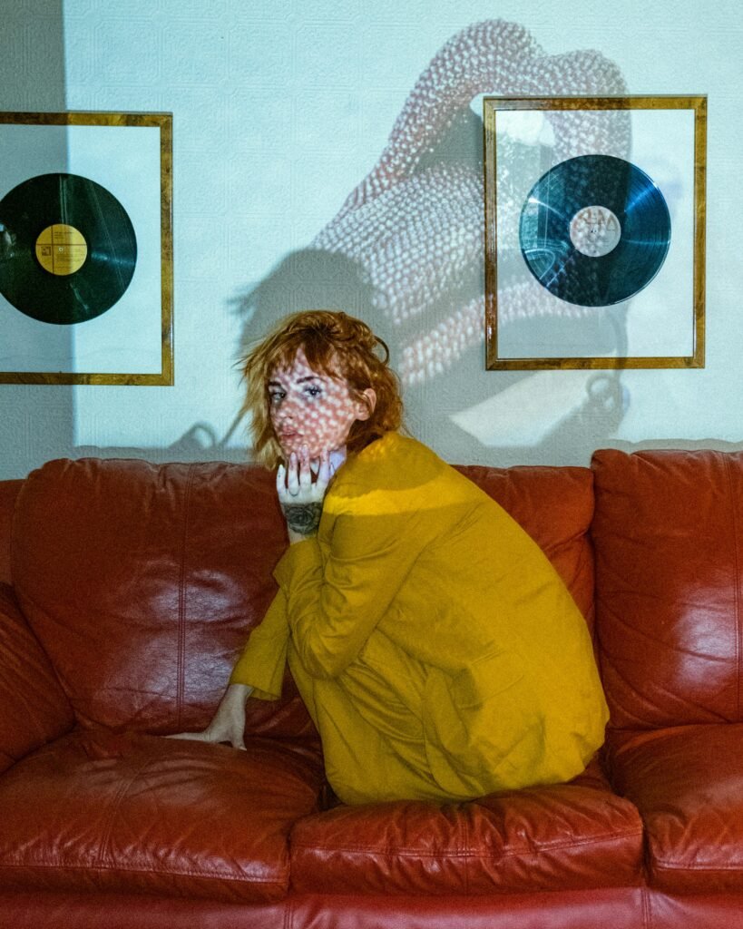 Artistic portrait of a woman sitting on a couch with projected patterns and vinyl decor.