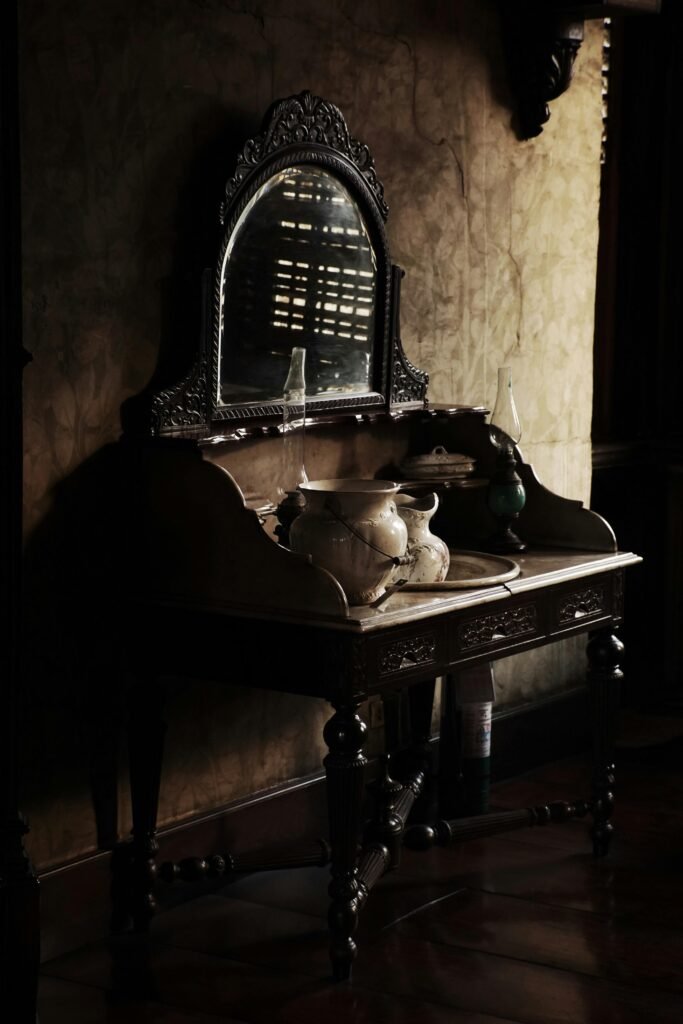 Antique wooden vanity with mirror and decorative pottery, creating a moody vintage interior scene.