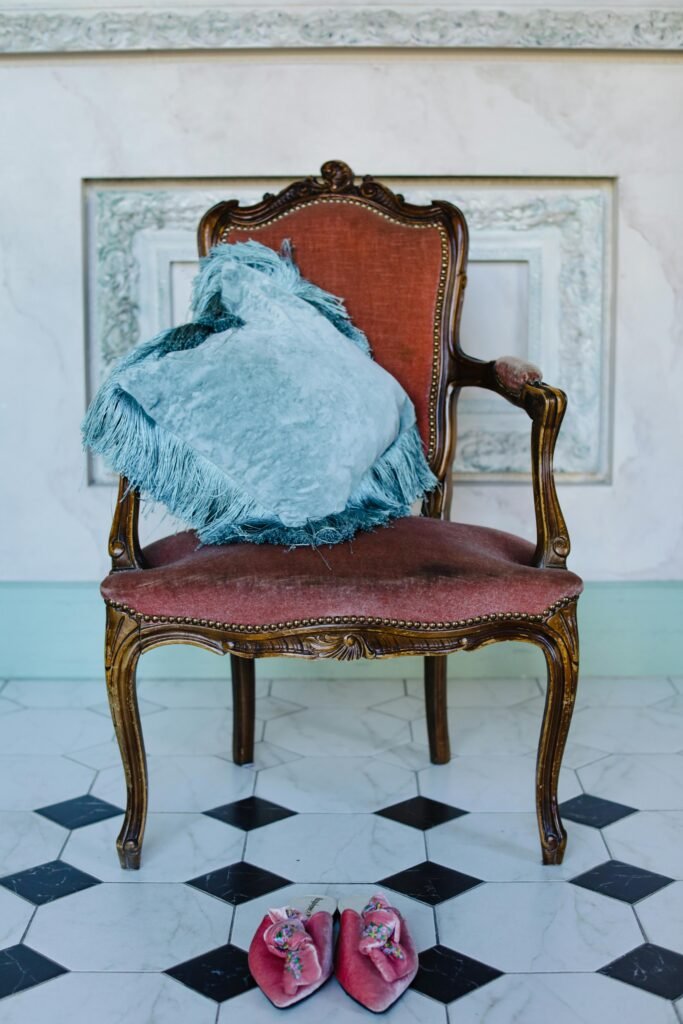 Elegant vintage armchair adorned with a throw pillow and decorative mules on a tiled floor.